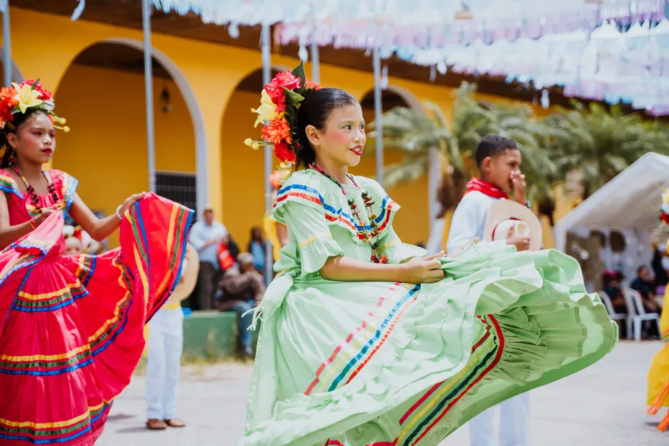 Niñas y niños bailan con vestuario tradicional en una presentación al aire libre